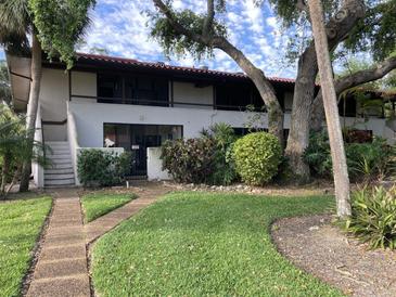 Two story condo with red tile roof, green lawn, and mature trees in a lush landscaped setting at 3500 El Conquistador Pkwy # 129, Bradenton, FL 34210