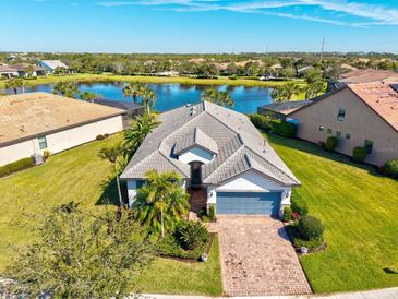 Stunning aerial view of a lakeside home with a beautiful tile roof, brick driveway, and lush landscaping at 5590 Rain Lily Ct, Sarasota, FL 34238