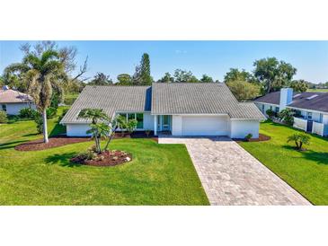 Charming single-story home boasting a manicured lawn, brick driveway, and tropical landscaping with mature palm trees at 3725 Spyglass Hill Rd, Sarasota, FL 34238