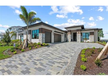 Modern home with a paver driveway, three-car garage, and meticulously landscaped front yard with palm tree at 800 Blue Shell Loop, Sarasota, FL 34240