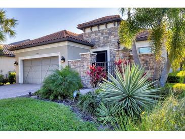 Charming home featuring a stone facade, tile roof, well-manicured landscaping, and a welcoming entrance gate at 9914 Craftsman Park Way, Palmetto, FL 34221