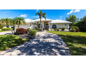 Inviting single-story home with a paver driveway, lush landscaping, and a pristine white tile roof at 832 Carnoustie Dr, Venice, FL 34293