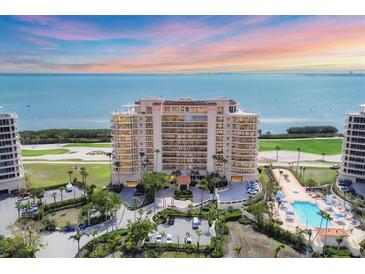 Stunning waterfront condo building with a pool, parking and landscaped grounds against a beautiful sky at 3030 Grand Bay Blvd # 323, Longboat Key, FL 34228