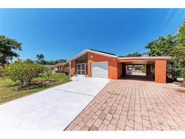 Charming orange home featuring an attached carport, screened in front porch, and spacious driveway at 3053 Monica Pkwy, Sarasota, FL 34234