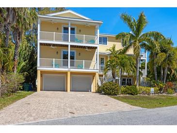Charming yellow two-story home featuring double balconies, two-car garage, and lush tropical landscaping at 306 Poinsettia Rd, Anna Maria, FL 34216