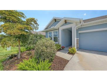 Charming home featuring a blue exterior, attached garage, and beautifully landscaped front yard with mature trees and flowering bushes at 8110 Trimbelle Ter, Parrish, FL 34219