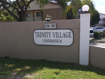 Entrance to Trinity Village Condominium complex with prominent signage and manicured landscaping at 2938 Clark Rd # 203, Sarasota, FL 34231