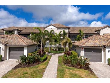 Beautiful condo exterior featuring lush landscaping, private garages, and a tiled roof against a bright sky at 5720 Palmer Cir # 103, Bradenton, FL 34211