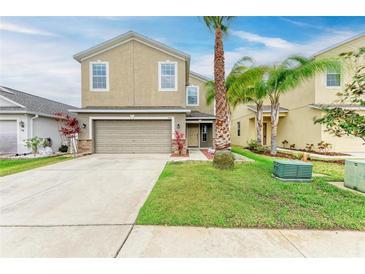 Two story home featuring a two-car garage, neutral stucco, manicured lawn and tropical landscaping with palm trees at 1912 Hawks View Dr, Ruskin, FL 33570