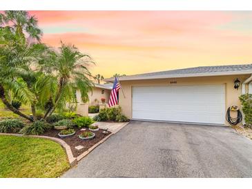 Charming home featuring lush landscaping, palm trees, and a welcoming two-car garage at 6940 W Country Club N Dr # V-77, Sarasota, FL 34243
