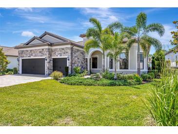 Elegant single-Gathering home featuring stone accents, a three-car garage, and lush tropical landscaping at 8033 Grande Shores Dr, Sarasota, FL 34240