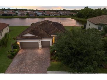Beautiful waterfront home with a two-car garage and a brick driveway in a lush, landscaped neighborhood at 3512 Scrub Creek Run, Lakewood Ranch, FL 34211