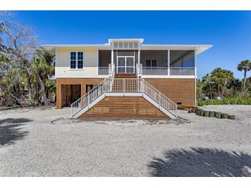 Beautiful elevated home with a double staircase, light yellow siding and covered area underneath at 32 Palm Dr, Placida, FL 33946