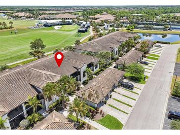 Aerial view of condo building with golf course and pond nearby, featuring tiled roof and well-manicured landscaping at 5528 Palmer Cir # 204, Lakewood Ranch, FL 34211