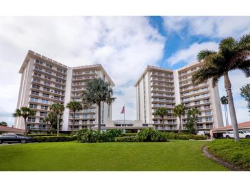 Bright, multi-story building complex with lush landscaping, palm trees, and an American flag under a blue sky at 2301 Gulf Of Mexico Dr # 36N, Longboat Key, FL 34228