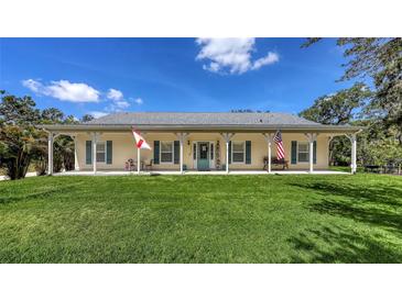 Charming single-story home featuring a large porch, green lawn, and a cheerful blue front door at 6365 Jim Davis Rd, Parrish, FL 34219