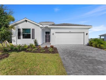Charming single-story home with a manicured lawn, a gray driveway and a two-car garage under a clear sky at 8134 Shore Lake Dr, Englewood, FL 34224