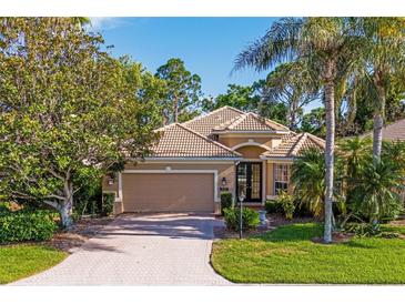 Charming single-story home with a tile roof, lush landscaping, and a brick driveway at 9120 Willow Brook Dr, Sarasota, FL 34238