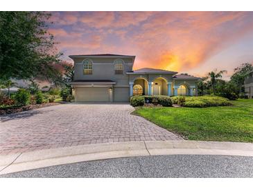 Charming two-story home with lush landscaping, a paver driveway, and a tile roof set against a colorful sunset at 12838 Daisy Pl, Bradenton, FL 34212