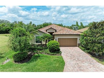 Beautiful single-story home featuring a terracotta-tiled roof, paver driveway, and lush tropical landscaping at 157 Wandering Wetlands Cir, Bradenton, FL 34212