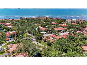 An aerial view of a charming community with lush trees, red roofs, and a view of the beautiful blue ocean in the background at 3803 Sun Eagle Ln # 203, Bradenton, FL 34210