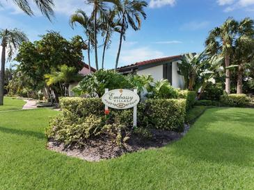 Landscaped community entrance sign for Embassy Villas with tropical landscaping in a sunny setting at 800 S Blvd Of The Presidents # 19, Sarasota, FL 34236