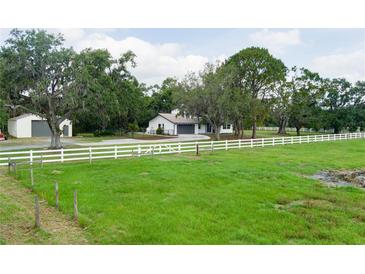 Sprawling home exterior featuring a white fence, large trees, and a detached garage at 5403 Red Rooster Rd, Parrish, FL 34219