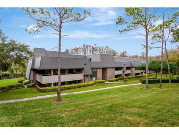 Low angle exterior of gray two-story condominium building on grassy hill with trees at 36750 Us 19 N # 03102, Palm Harbor, FL 34684