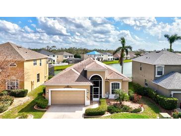 Stunning aerial view of tan house with lush landscaping and a serene waterfront backyard at 8995 Founders Cir, Palmetto, FL 34221