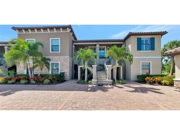 Beautiful condo building featuring lush landscaping, a paver driveway, and elegant architectural details under a bright blue sky at 12720 Sorrento Way # 103, Bradenton, FL 34211