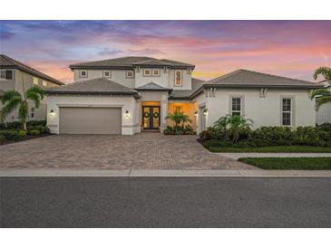 Elegant home featuring a brick driveway, tropical landscaping, and a two-car garage set against a vibrant sunset backdrop at 6152 Lungo Lago Dr, Sarasota, FL 34241