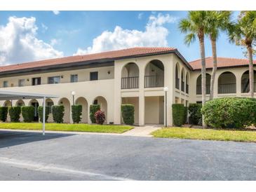 Beige two-story condominium building with arched entryways, red tile roof, trimmed bushes, and black parking lot at 3690 Pinecrest St # 114, Sarasota, FL 34232