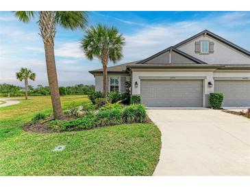 Green lawn leads to a two-car garage, with lush landscaping with palm trees in front of the townhome at 6094 Amberly Dr, Bradenton, FL 34208
