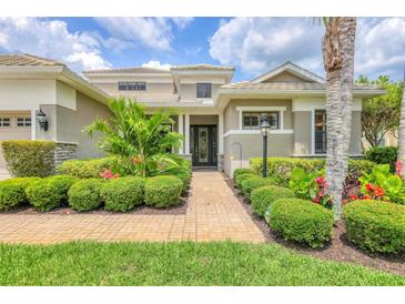 Beautifully landscaped single Gathering home with beige exterior, palm trees, and brick paver walkway at 6470 Indigo Bunting Pl, Lakewood Ranch, FL 34202
