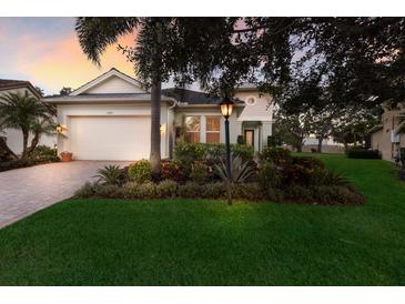 Charming single-story home featuring a manicured lawn, paver driveway, and lush landscaping with elegant exterior lighting at 13848 American Prairie Pl, Lakewood Ranch, FL 34211