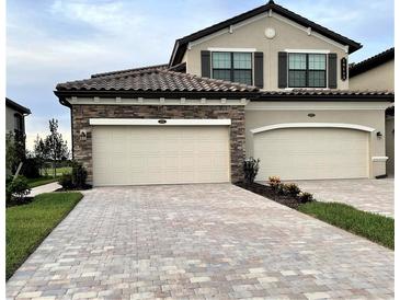 Inviting home featuring a stone facade, brick paver driveway, and a two-car garage at 18113 Gawthrop Drive # 101, Lakewood Ranch, FL 34211