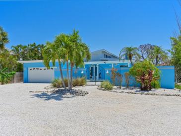 Charming single-story blue home with a well-manicured front yard and rock landscaping with palm trees at 5920 Gulf Of Mexico Dr, Longboat Key, FL 34228