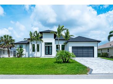 Beautiful modern home with lush lawn, palm trees, dark roof, and paver driveway at 117 Marker Rd, Rotonda West, FL 33947