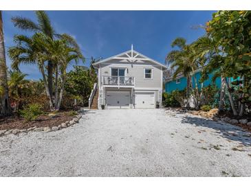 Charming two-story home with a white gravel driveway, lush landscaping, and a light gray facade at 799 Jacaranda Rd, Anna Maria, FL 34216