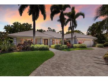 Stunning home showcasing palm trees, meticulous landscaping, and a paver driveway, set against a colorful sunset sky at 1780 Pine Harrier Cir, Sarasota, FL 34231
