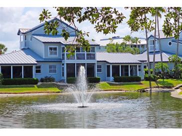 Water view of this gray two-story home, with a fountain, grassy lawn, and mature shrubbery at 1311 Siesta Bayside Dr # 1311-A, Sarasota, FL 34242