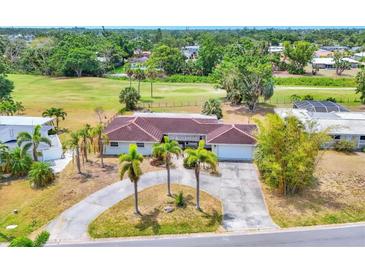 Expansive single-story home with a red tile roof, surrounded by lush greenery and a circular driveway at 3432 Pine Valley Dr, Sarasota, FL 34239