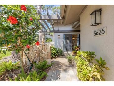 Inviting front entrance with a stone pathway, lush landscaping, and a pergola, leading to a glass-paneled front door at 5626 Pipers Waite # 22, Sarasota, FL 34235