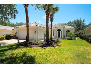 Beautiful single-story home with a well-manicured lawn and lush landscaping, including mature palm trees at 5877 Ferrara Dr, Sarasota, FL 34238