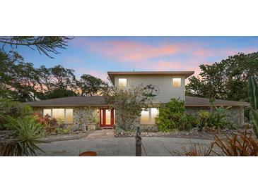 Charming home featuring a stone facade, red door, and lush, tropical landscaping at 8255 Longbay Blvd, Sarasota, FL 34243