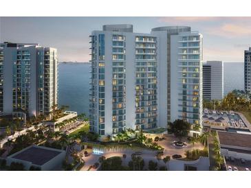 Luxury high-rise condominium with a circular driveway, lush landscaping, and partial ocean views at 555 Quay Cmn # 1005, Sarasota, FL 34236