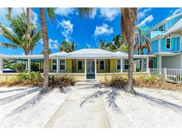 Charming yellow beach house with white trim, surrounded by palm trees and sandy landscape at 104 Magnolia Ave, Anna Maria, FL 34216