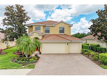 Two-story home featuring a tile roof, three-car garage, brick driveway, and professionally landscaped yard at 235 River Enclave Ct, Bradenton, FL 34212