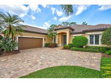 Charming tan home with a brick driveway, a tile roof, and lush landscaping with palm trees at 4818 88Th E St, Bradenton, FL 34211