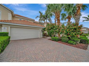 Two-car garage on a home with a red tile roof, brick driveway, and tropical landscaping at 23233 Banbury Way # 302, Venice, FL 34293